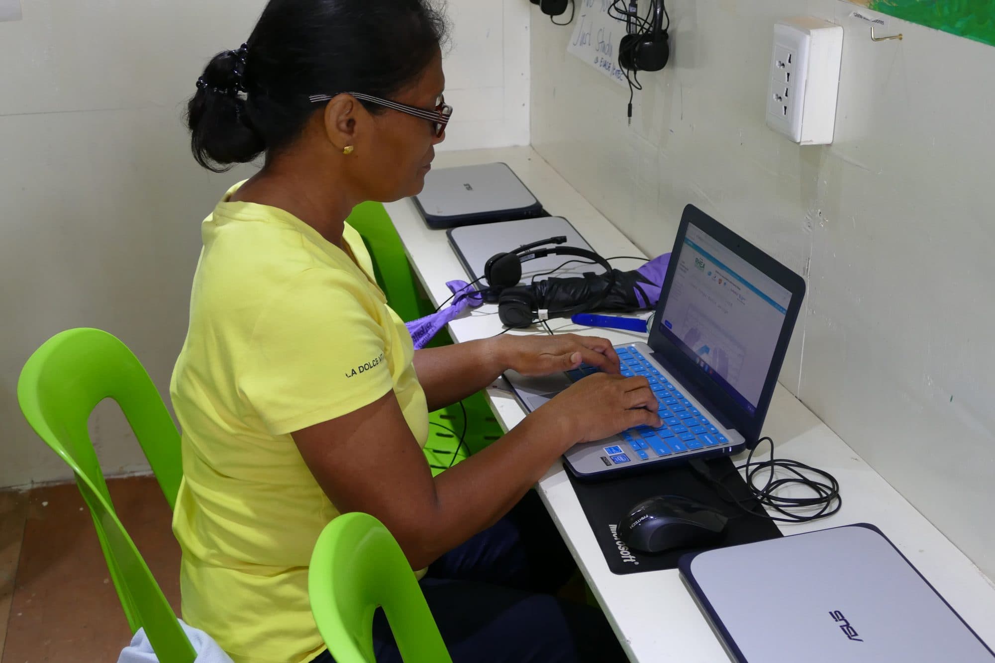 An adult learner types at a laptop in the container classroom