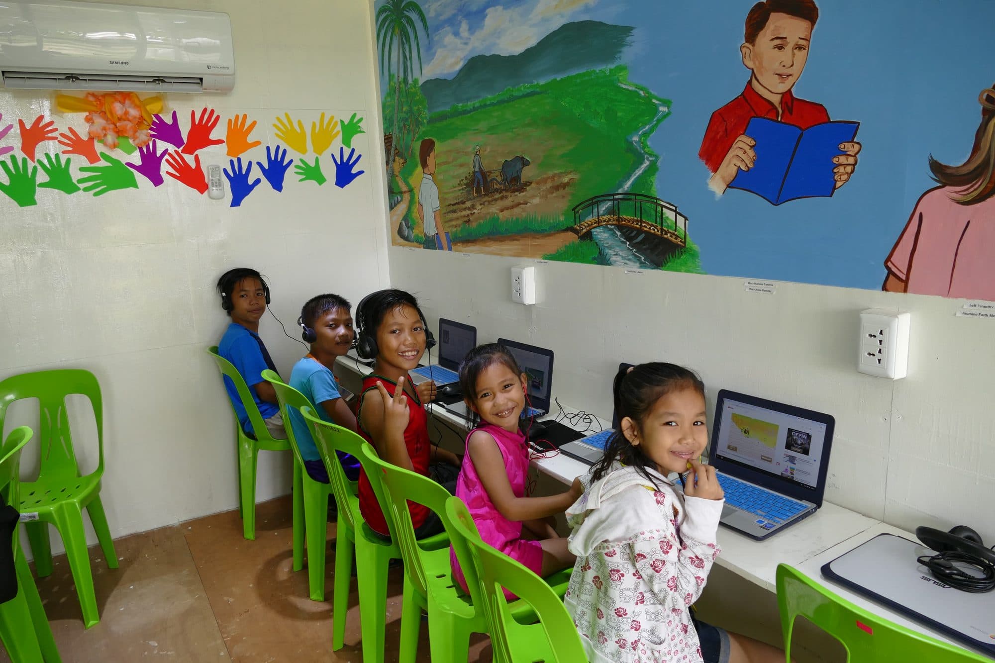 Young students at laptops in the container classroom smile at the camera