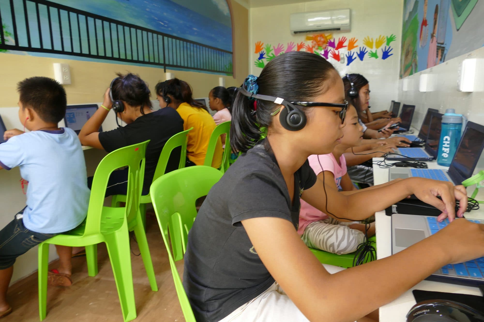A student with headphones types at a laptop in the container classroom