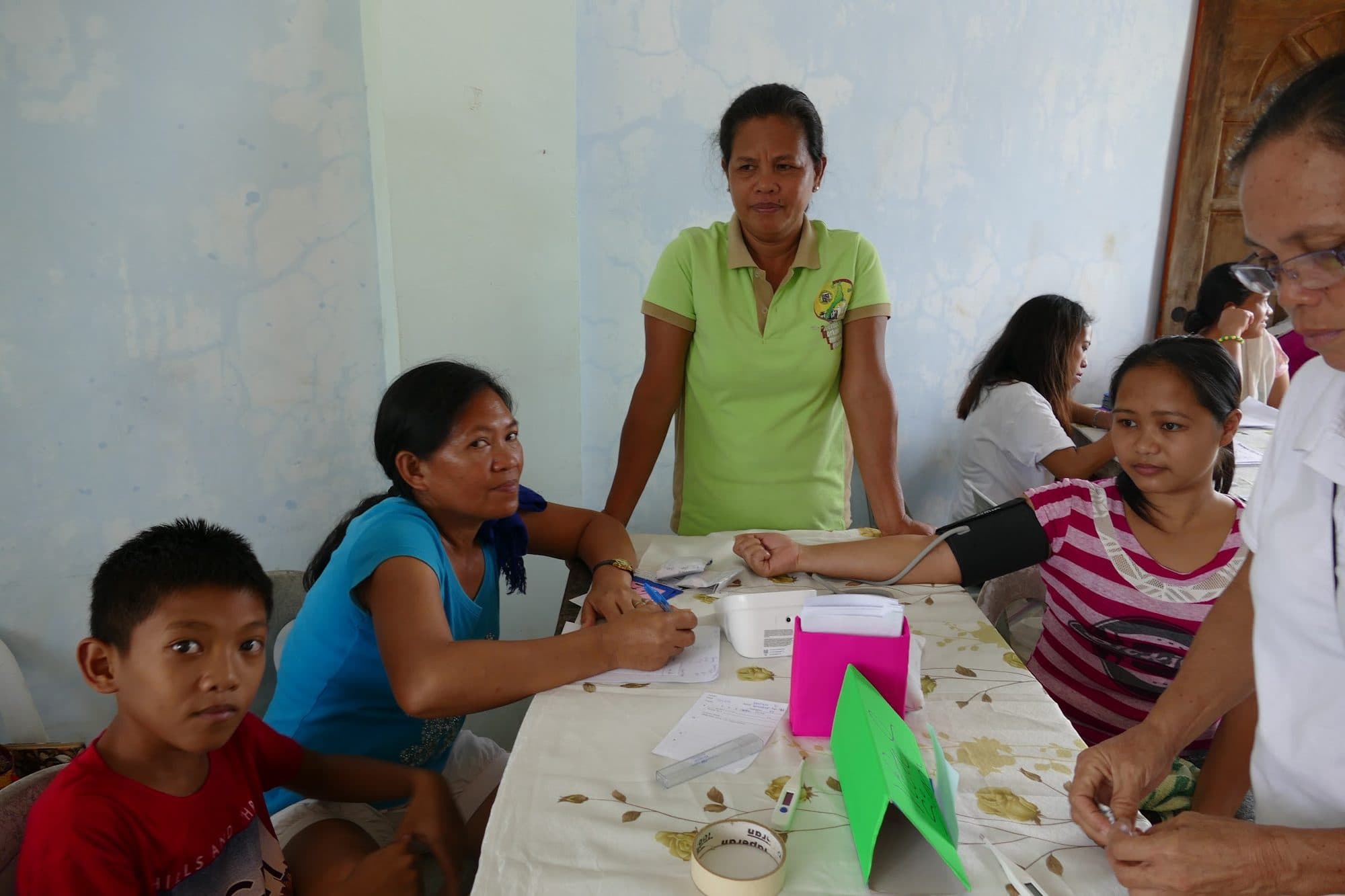 A clinic worker takes a blood pressure reading while families wait at the table