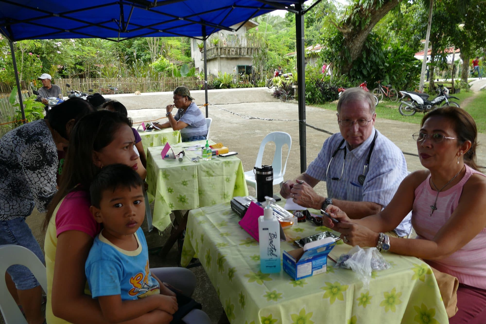 Families and clinic staff at a table under a tent at a traveling clinic