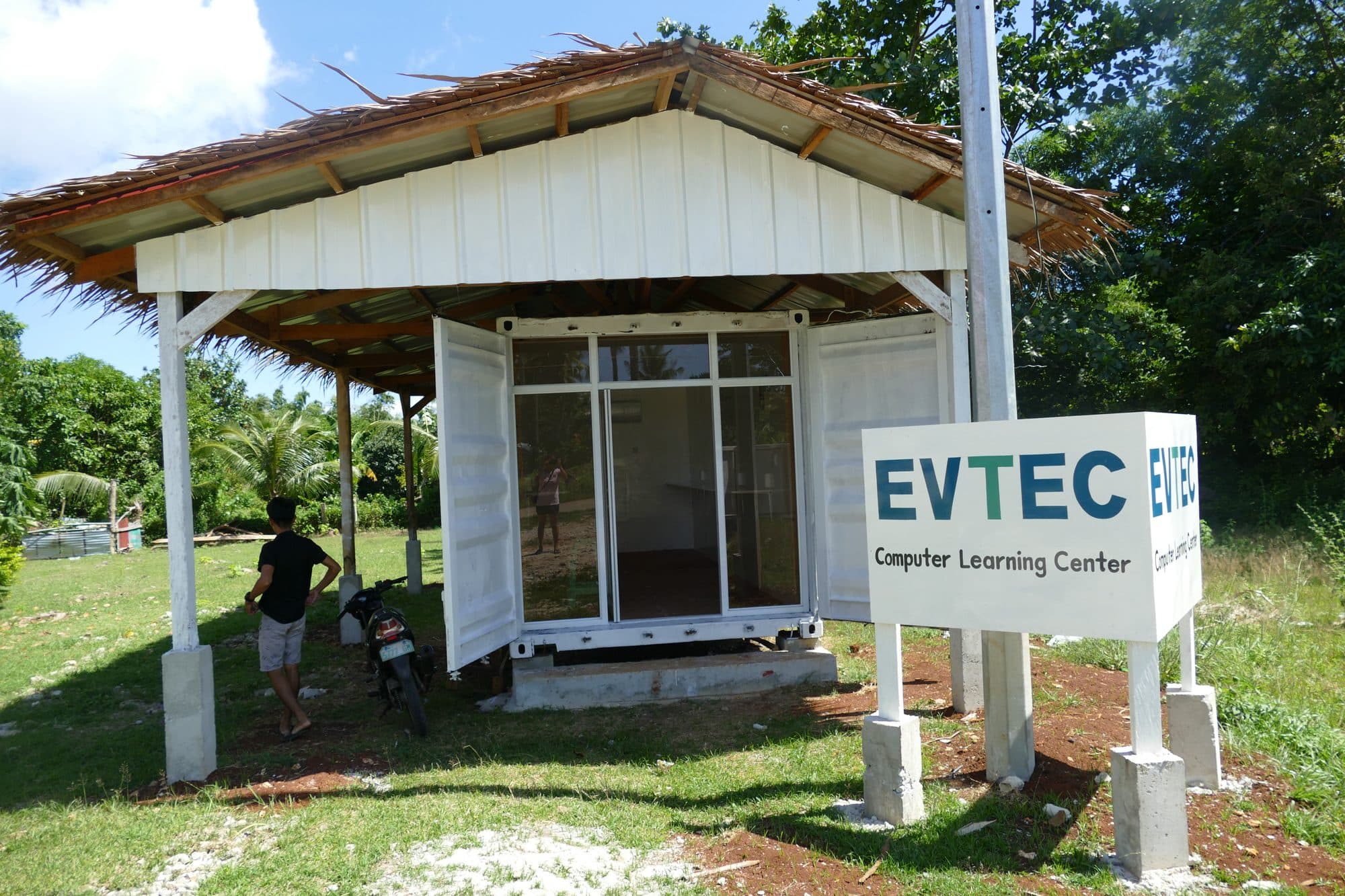The learning center, a white shipping container under a thatched roof, with the EVTEC sign in front