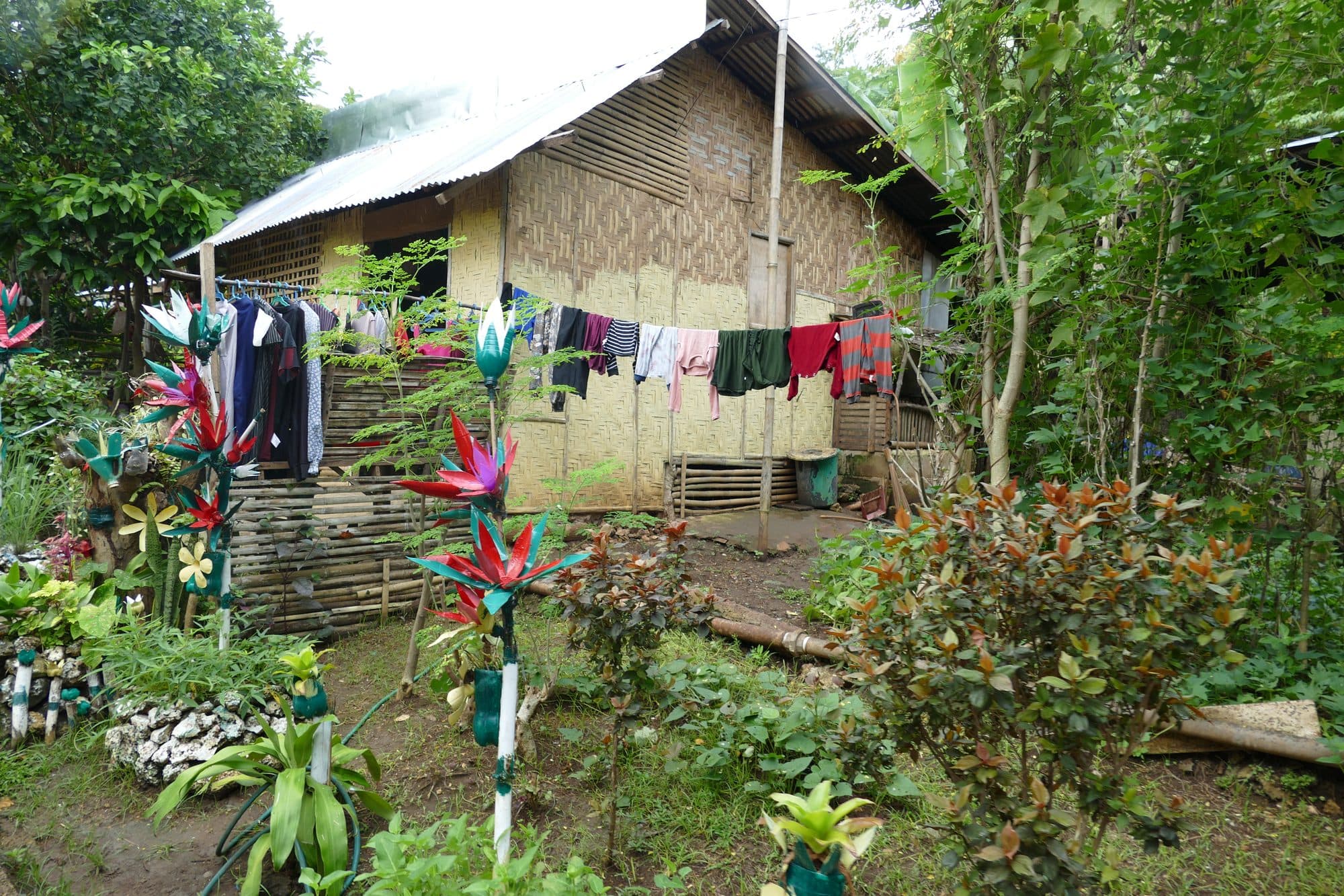 A bamboo house with laundry on the line and a flower garden