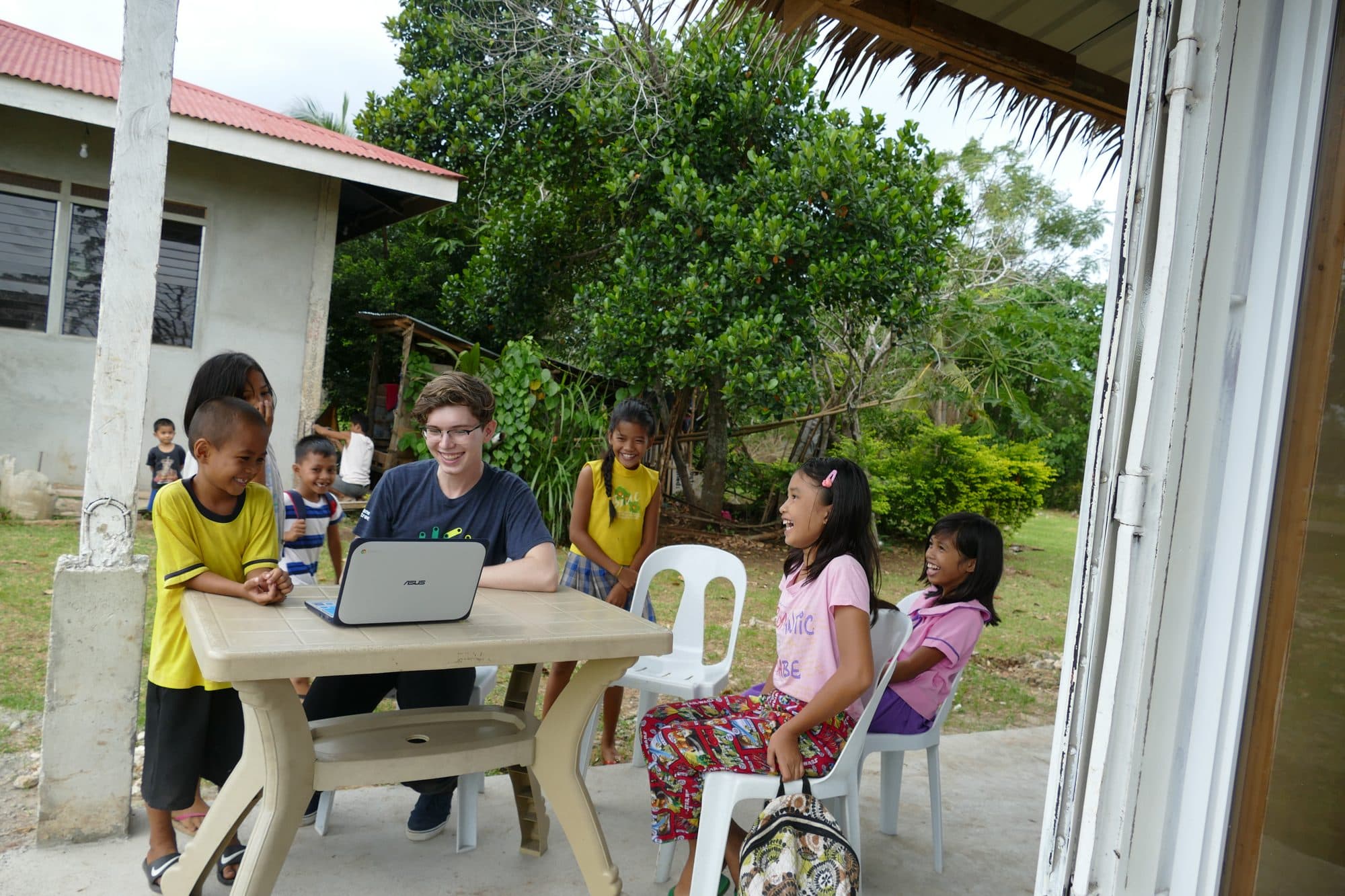Children gathered around a laptop at a table outside the center