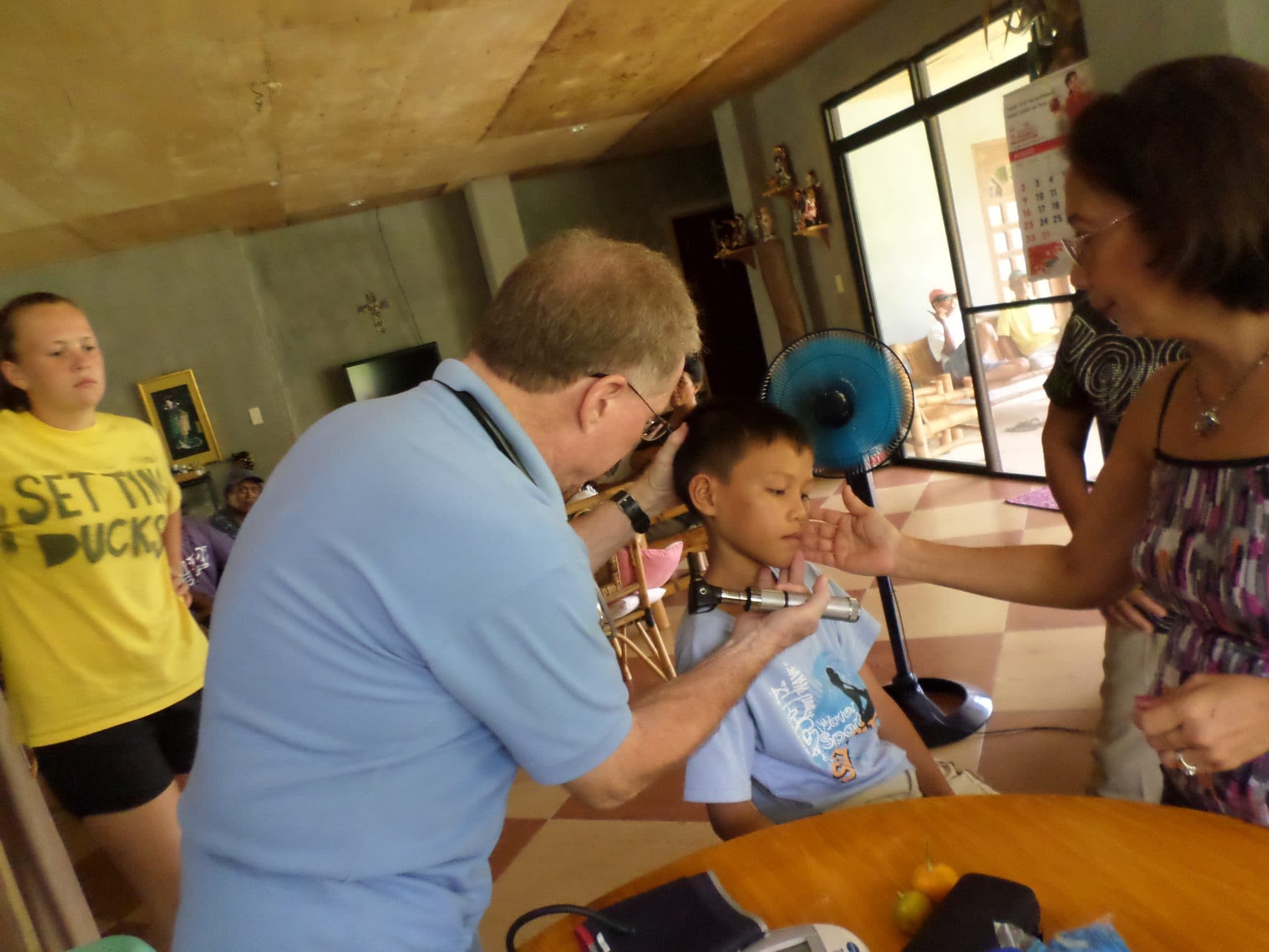 A clinician looks in a boy's ear while a volunteer and the boy's mother watch