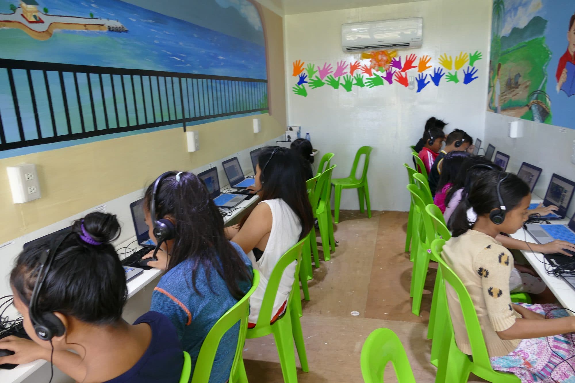 A row of students with headphones at laptops inside the container classroom