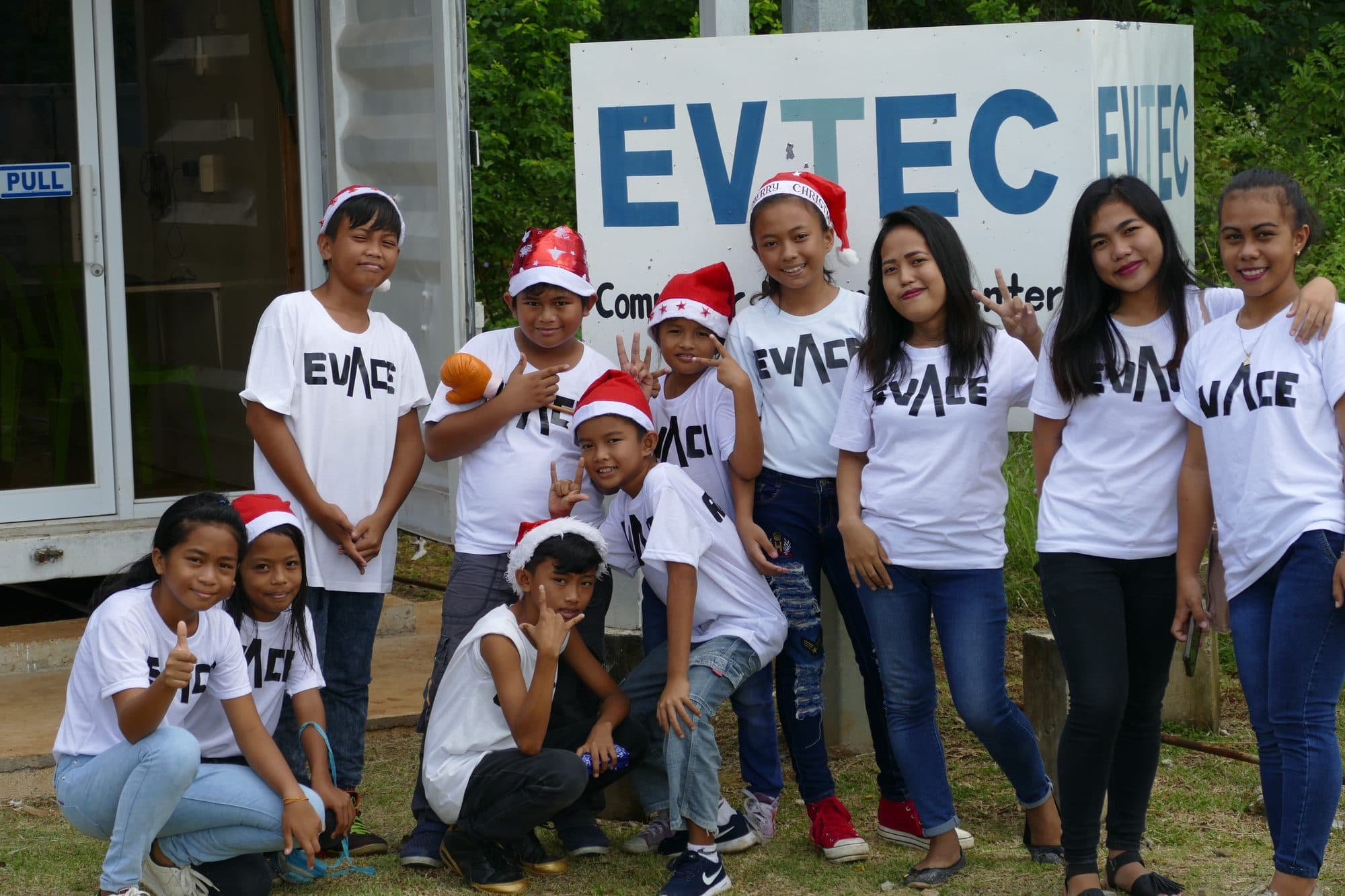 Students in EVACE shirts and Santa hats in front of the EVTEC sign