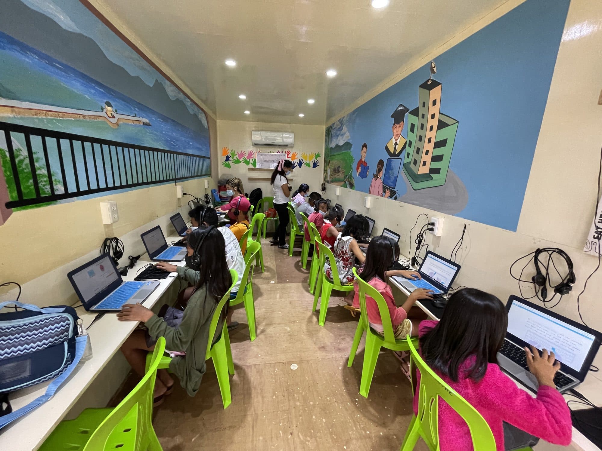 Students at laptops down both sides of the container classroom